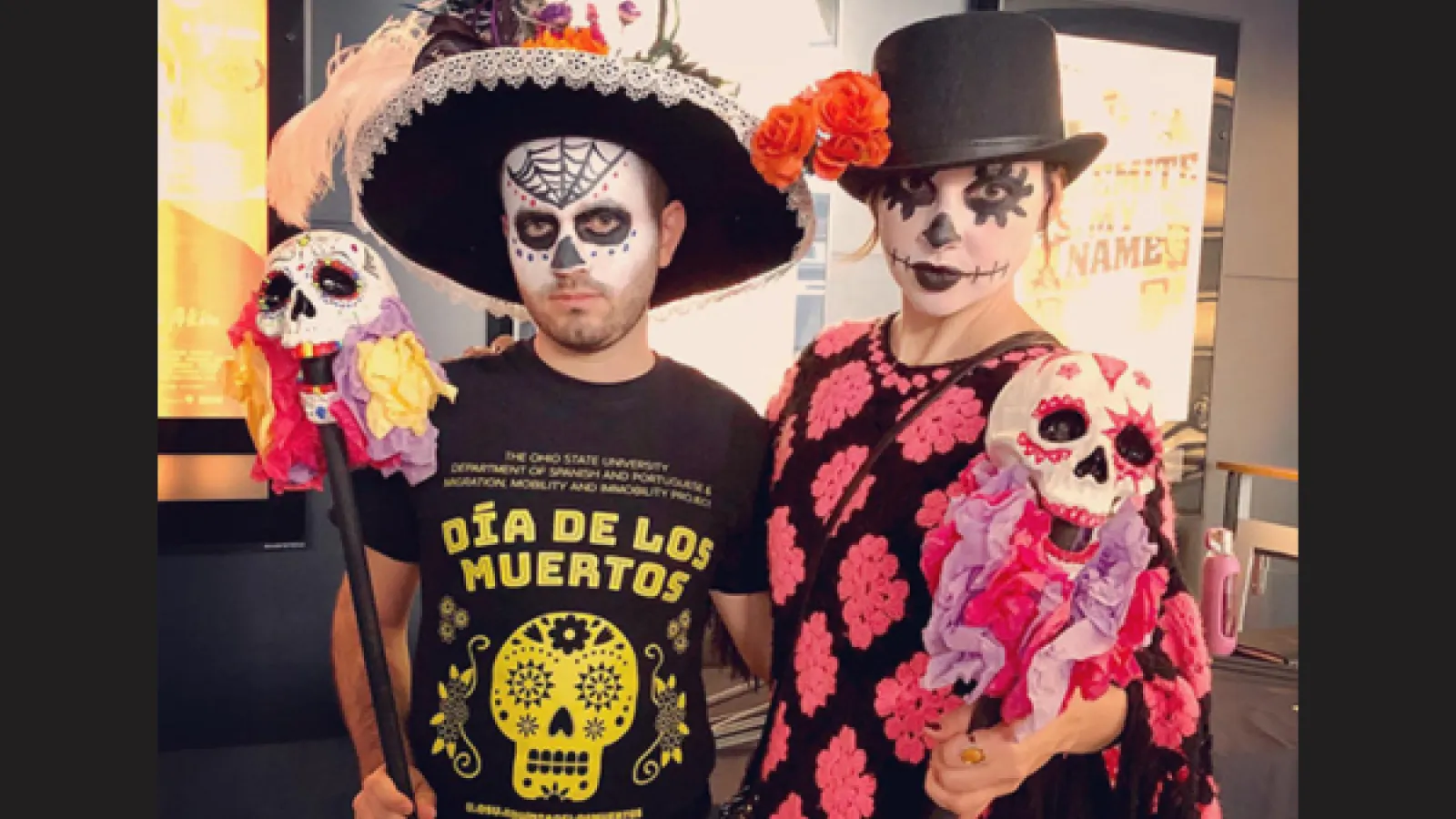 A man has a skull painted on his face and a woman is wearing a top hat