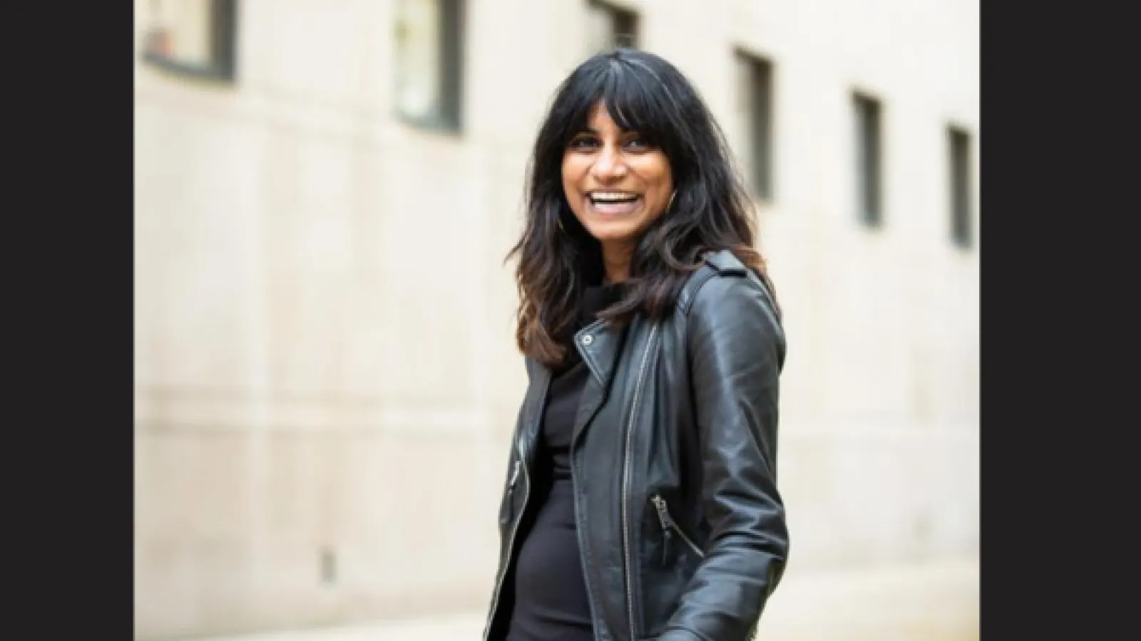 A woman wearing a leather jacket with long brown hair, she is smiling