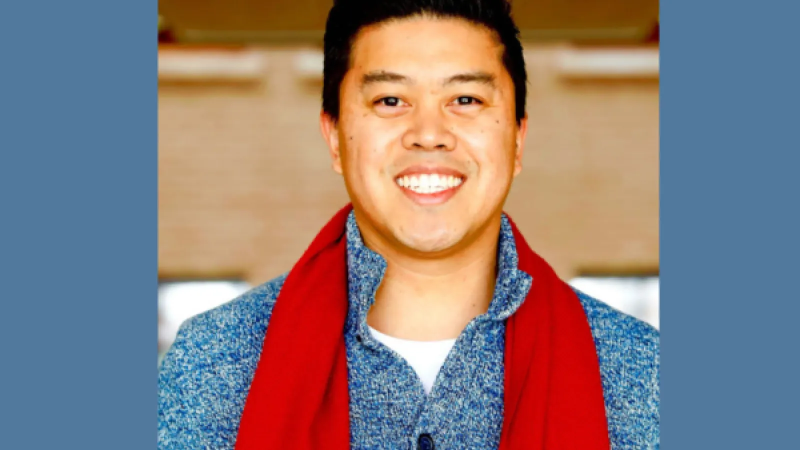 An asian man smiling and wearing a bright red scarf